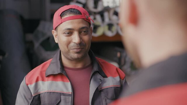 Medium close-up of smiling middle-eastern stockroom workman in uniform drinking coffee from plastic cup talking to colleague at lunchtime with construction materials in background