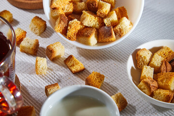 Square toasted pieces of homemade delicious rusk, hardtack, Dryasdust, zwieback, Liquid honey in a saucer, glass of milk and black tee in a cap on a white tablecloth.