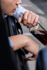 cropped view of man holding bottle of whiskey in car on blurred foreground, banner.