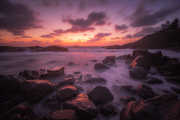 A landscape of the sea with long exposure surrounded by rocks during a breathtaking sunset
