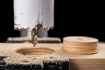 Drilling metal hole saw in a piece of wood. Making holes in a carpentry workshop.