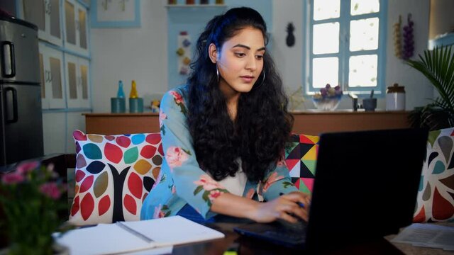 Confident college-going girl taking down notes from a laptop - remote learning. Medium shot of a young attractive lady watching her lessons on the computer screen and making notes - online studies