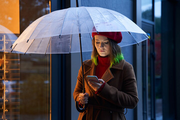 Girl outdoor with umbrella using smart phone