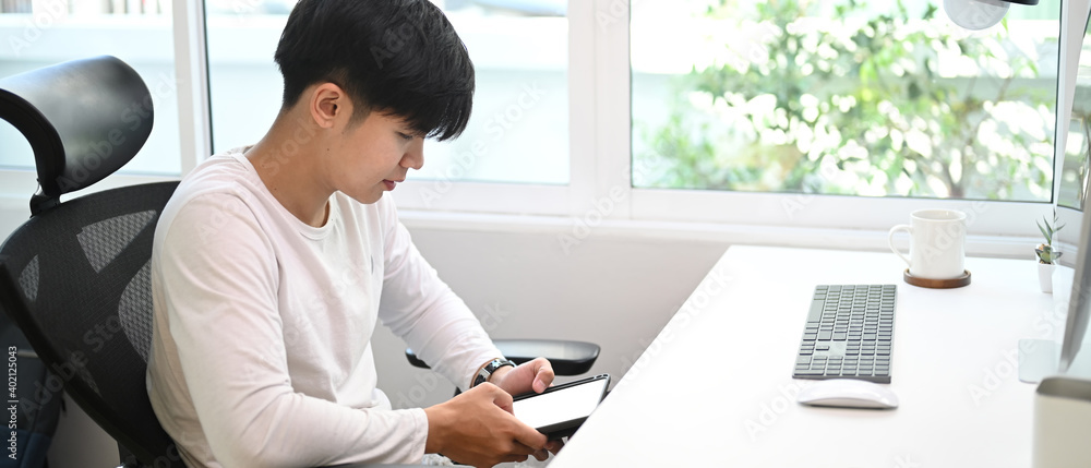Poster horizontal image of freelance man sitting in front of computer and using smart phone in home office.