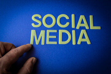 Human finger pointing the words Social Media written with plastic letters on blue paper background, concept