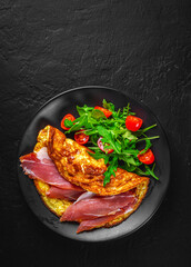omelette with prosciutto and salad on black plate on Dark grey black slate background