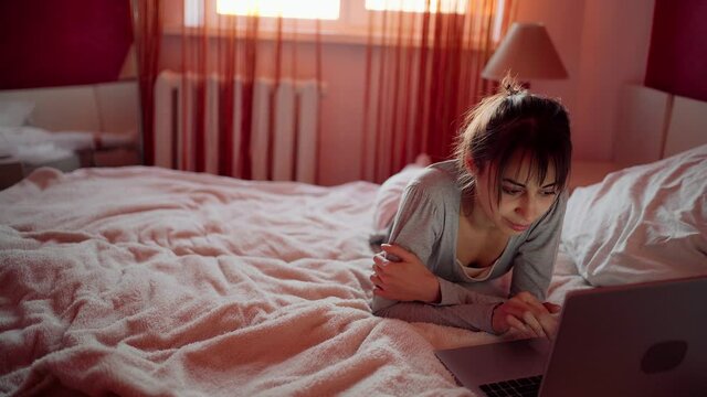 Young woman lying on bed at home and watching laptop computer, browsing on Internet, reading news, searching information in social networks. Stay at home and quarantine concept.