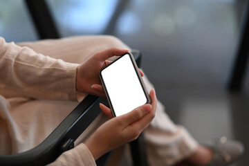 Close up view of businesswoman using mock up smart phone with white screen while sitting in her workspace.