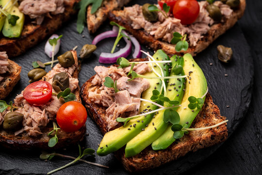 Set of bruschettas with tuna, quail egg, cherry tomatoes, avocado, microgreen and capers on a light background, Toasts with tuna delicious healthy food. top view