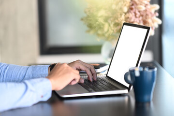 Side view man hands typing on keyboard of mock up laptop computer with blank screen.