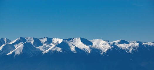 Beautiful winter panoramic mountain landscape. The white snowy peaks of Pirin Mountains, viewed from The Rila Mountains in Bulgaria, blue sky. Snowy weather conditions for winter sports and tourism.