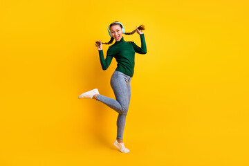 Full length body size view of pretty cheerful girl listening music jumping dancing isolated on bright yellow color background