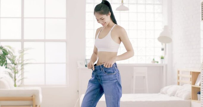 
Young slim woman in  big jeans showing her diet results at home