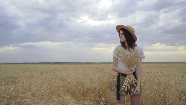 Young girl in a straw hat stands in a wheat field.
