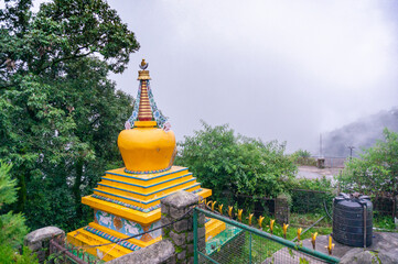 Yellow temple spire dome building perched in the middle of trees looking over a cloudy foggy valley in a hillstation like Mcleodganj shimla and more a popular tourist and homestay destination