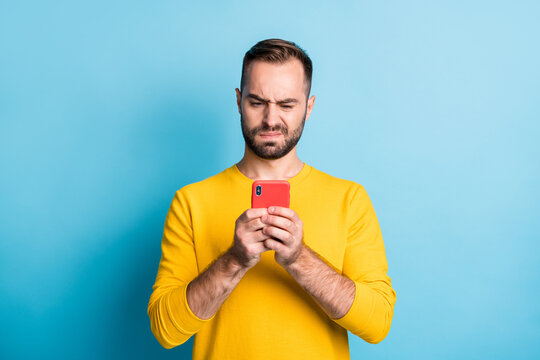 Photo of young unhappy upset sad unsure uncertain man see dislike bad comment in phone isolated on yellow color background