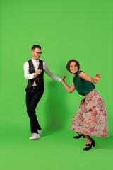 Party. Old-school fashioned young woman dancing isolated on green studio background. Artist fashion, motion and action concept, youth culture, fashion returning. Young stylish man and woman.