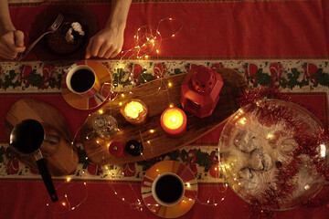 Christmas table with coffee, lights, candles. Man eats a cookie and drinks coffee