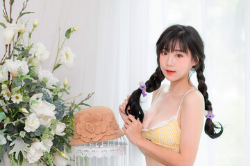 Obraz premium A beautiful and cute woman, she is Asian, Thai, she is wearing a yellow bikini, smiling and holding her hair.