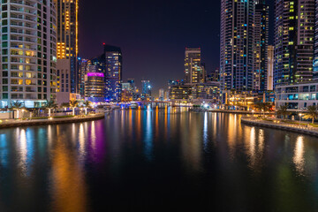 Fototapeta premium Night view to Dubai Marina panorama, reveals Pears 7, skyscrapers and beautiful bridge. Luxury destination for tourists and residents. Amazing colors reflect on the water. 