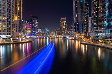Fototapeta na wymiar Night view to Dubai Marina panorama, reveals Pier 7, skyscrapers, speed boat light trails and beautiful bridge. Amazing colors reflect on the water.