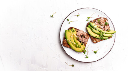 Tuna sandwiches with avocado and microgreen on wholemeal bread, wooden background. Tasty tuna sandwiches for breakfast or snack. Top view, flat lay, copy space