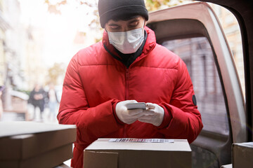 Courier in mask holding smartphone while scanning a barcode