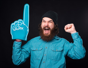 Amazed bearded hipster man pointing with fan glove and celebrating victory of favorite team.