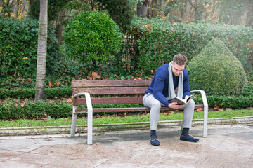 Fototapeta premium young man sitting on a park bench reading a book