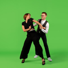 Rock n roll. Old-school fashioned young woman dancing isolated on green studio background. Artist fashion, motion and action concept, youth culture, fashion returning. Young stylish man and woman.