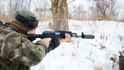 Submachine gun with a silencer during shooting, a shooter with headphones removed in a military...