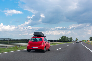 Red car with roof luggage box for travel on highway