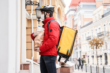 Courier wearing protective mask and gloves standing is under the door