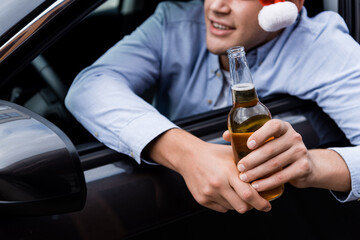 partial view of man looking out car window while holding whiskey, blurred background.