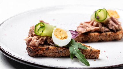 Italian bruschetta sandwiches with canned tuna, cucumber, quail eggs and onions, Toasts with tuna. Delicious breakfast or snack. Top view, flat lay, copy space