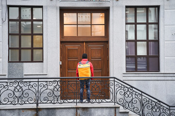Fototapeta na wymiar Delivery guy with termo backpack waiting for the door to open