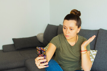 The girl sits on the couch and speaks on the phone. In a bad mood