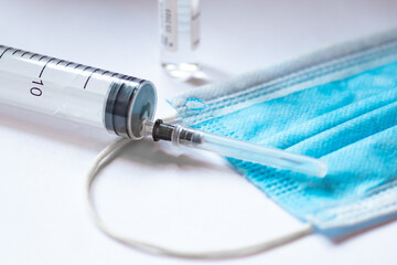 Syringe, vial and surgical face mask on a white table. Covid or Coronavirus vaccine background