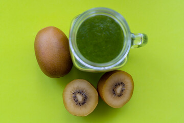 Colorful green fruit smoothie with fresh kiwis on green background.