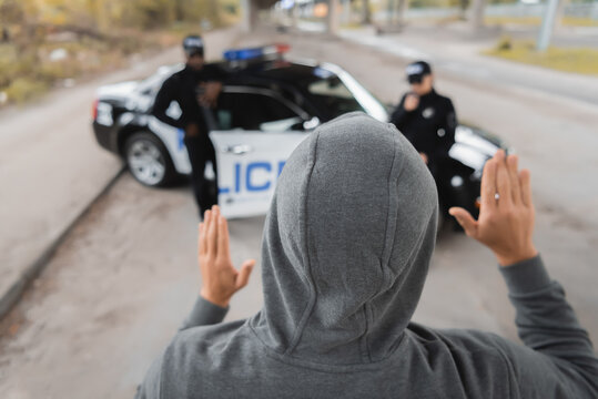 back view of hooded offender showing hands with blurred multicultural police officers on background outdoors.