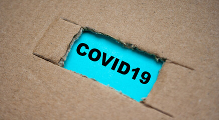 Fototapeta na wymiar cut-out hole in the paper cardboard, and under it a piece of paper with the word COVID19. The coronavirus news concept