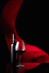Вottle and glass of red wine on a black reflective background.