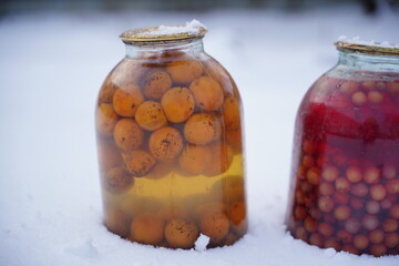 Close up of canned juice with fruits and berries in snow on street. Sealed jars of compote in garden in wintertime.