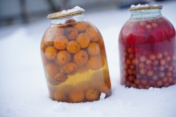 Close up of canned juice with fruits and berries in snow on street. Sealed jars of compote in...