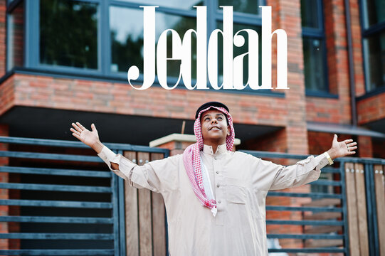 Jeddah - biggest city of Saudi Arabia. Middle Eastern saudi arabian man posed on street against modern building up his hands in the air.