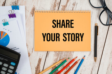 Notebook with text SHARE YOUR STORY near office supplies.
