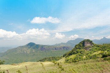 Single rock peak covered by trees and bushes with a background mountain range.
