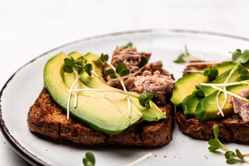 Sandwiches with avocado and tuna fish on wooden cutting board on white background, top view. Healthy breakfast or snack. Food recipe background. Close up