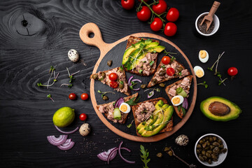 Fototapeta na wymiar Toasts with tuna. Italian Appetizer bruschetta, sandwiches with canned tuna, tomatoes and capers. delicious healthy food on a dark background, Top view