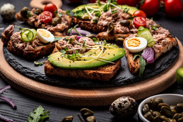 Sandwiches with avocado and tuna fish on wooden cutting board on black background, Healthy breakfast or snack. Long banner format, top view
